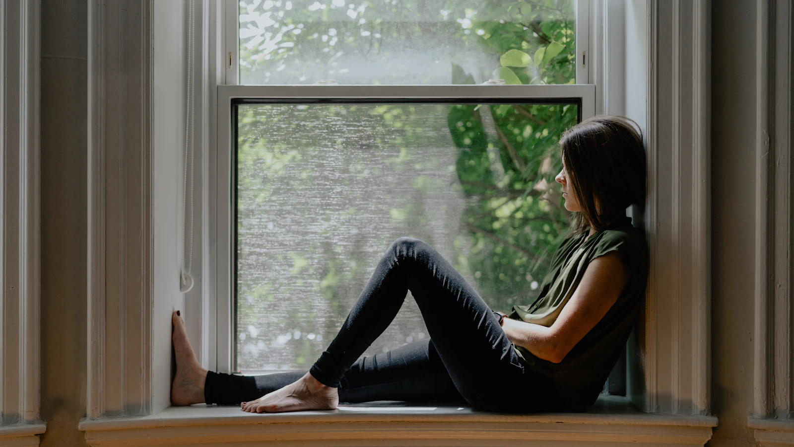 A woman sitting by a window looking outside